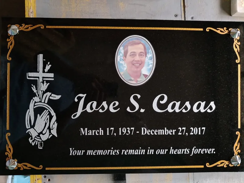 Black granite lapida with a gold border, silver script lettering, engraved cross and praying hands