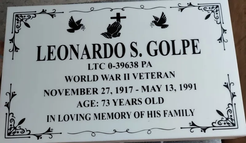 White marble lapida with black engraved lettering, doves, praying hands and a scroll border
