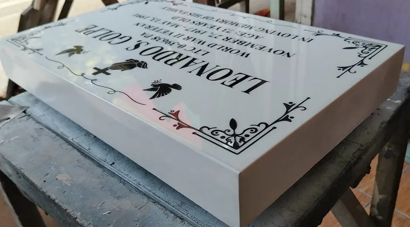 Angled view of a white marble lapida on the workshop bench, showing the stone's thickness and black engraved lettering